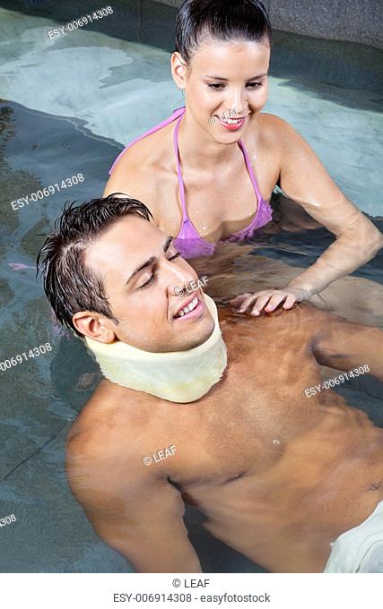 Young man wearing neck brace in pool with beautiful woman
