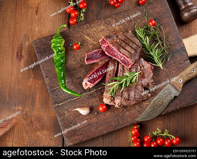 roasted piece of beef ribeye cut into pieces on a vintage brown chopping board, rare doneness. Delicious steak, top view