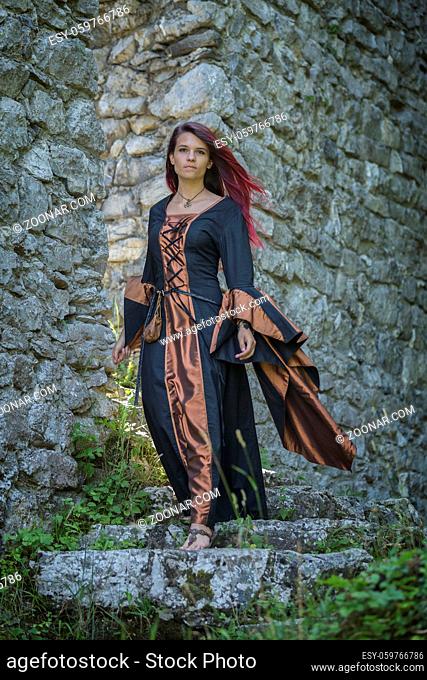 Junge rothaarige Frau in mittelalterlicher Kleidung eilt vom Eingang einer alten Burg hinunter ins Tal