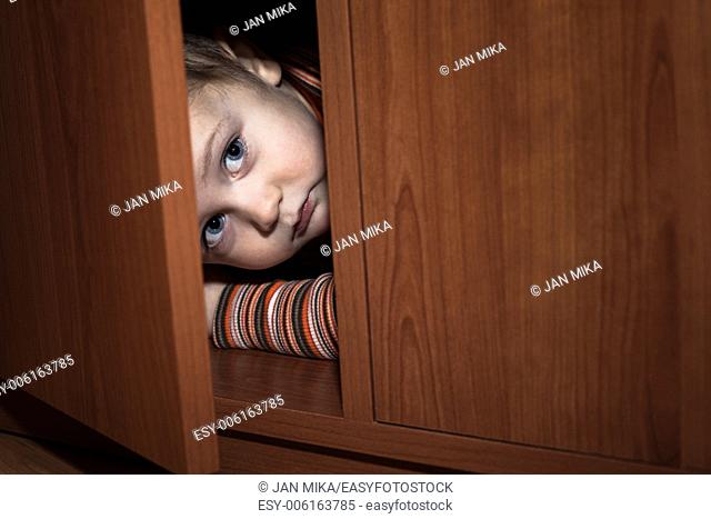 Scared child boy hiding in wardrobe