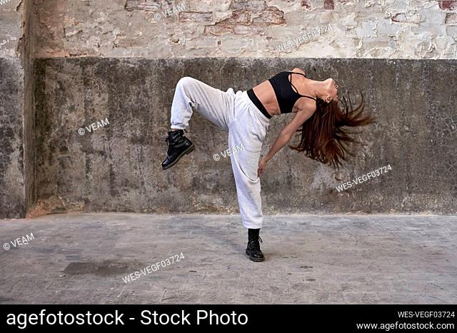 Female dancer dancing while hair tossed against wall in abandoned factory