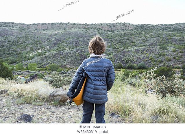 rear view of 6 year old boy holding folded camp chair looking at canyon wall