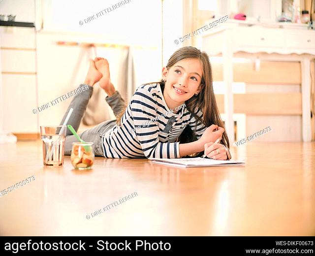 Smiling girl with book lying on floor at home