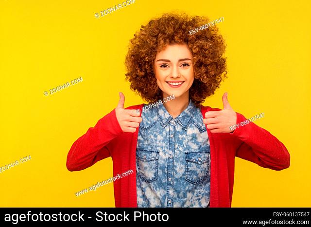 Like gesture. Happy successful woman with curly hair in casual style jeans shirt showing thumbs up, satisfied with excellent result, good feedback