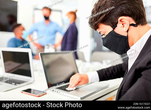 Junger Geschäftsmann mit Mundschutz beim desinfizieren der PC Tastatur