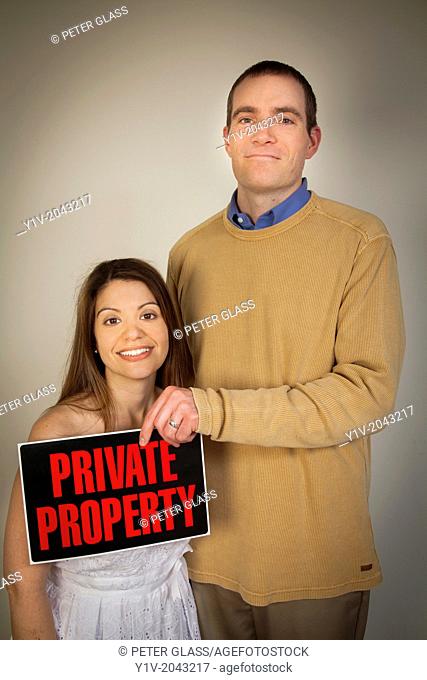 Young man holding a ""Private Property"" sign in front of his wife