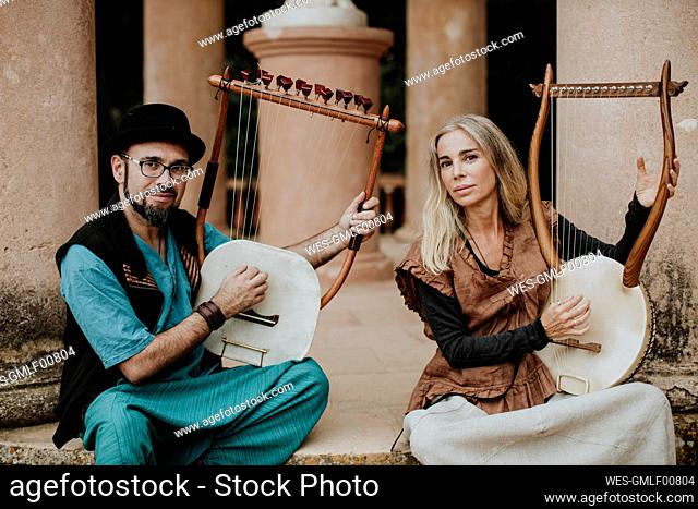 Confident female and male playing lyra musical instrument on staircase