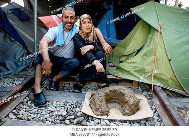 A married couple from Syria in the refugee camp of Idomeni in Greece at the frontier to Macedonia, April, 2016. Fireplace made of loam in the foreground