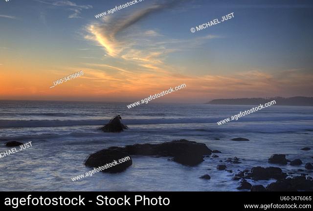Waves crash along the coastline during sunset near San Simeon, California