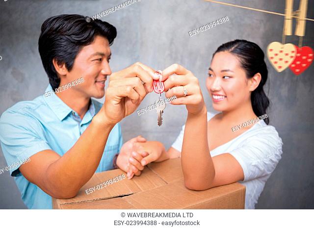 Hearts hanging on a line against happy couple holding house key and leaning on moving box