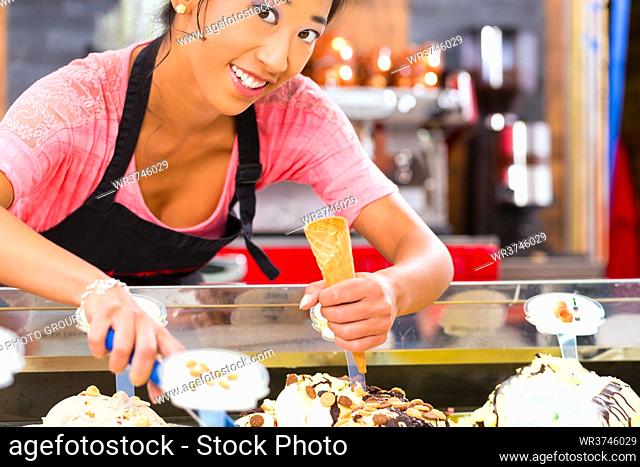 Young Asian saleswoman in an ice cream parlor takes a scoop of ice cream