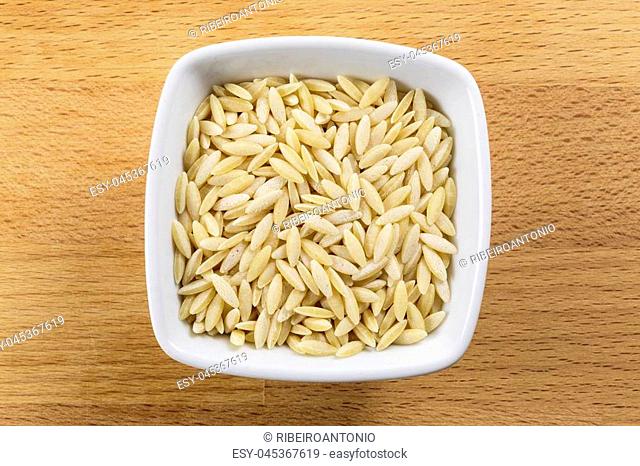 Overhead shot of raw pearl barley in a white bowl on a wooden chopping board background. Arborio rice is the main ingredient of the traditional Italian Risotto