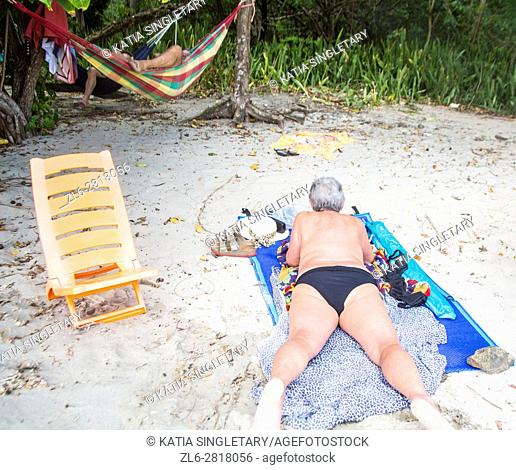 Topless mature senior woman laying on her towel on the beach in the tropical island of Martinique