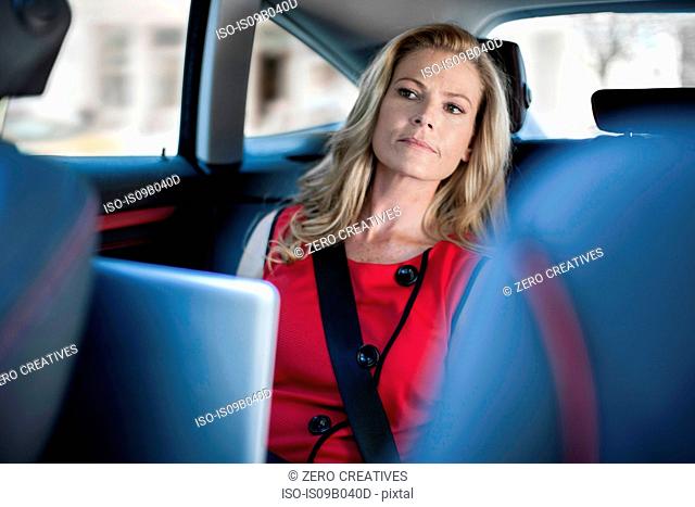 Businesswoman using laptop and looking from car back seat