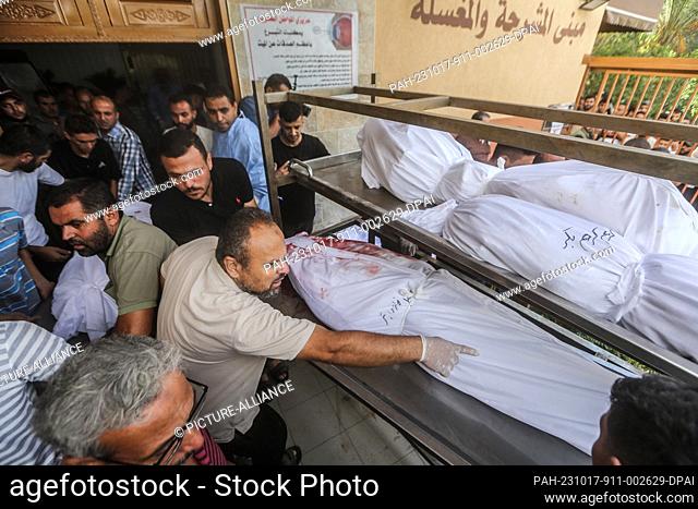 17 October 2023, Palestinian Territories, Khan Yunis: Palestinians stand with bodies wrapped in burial shrouds with their names written to identify them at...