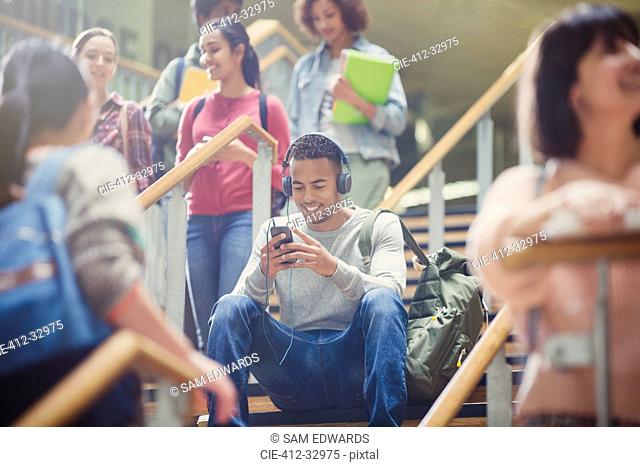 Male college student listening to mp3 player in busy stairway