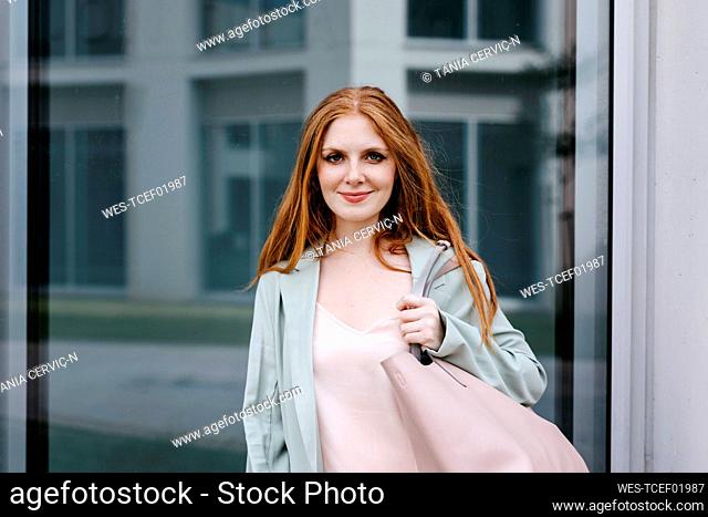 Beautiful redhead businesswoman with purse in front of window