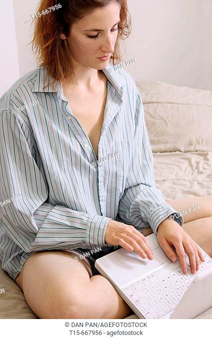 Red headed woman working on laptop on bed in pajamas