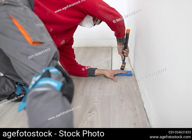 repairman laying flooring in apartment using a mask due to the corona virus pandemic