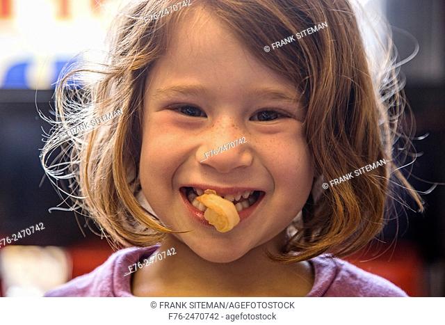 6 year old girl with a cooked shrimp in her mouth in a noodle restaurant in Berkeley, CA, USA