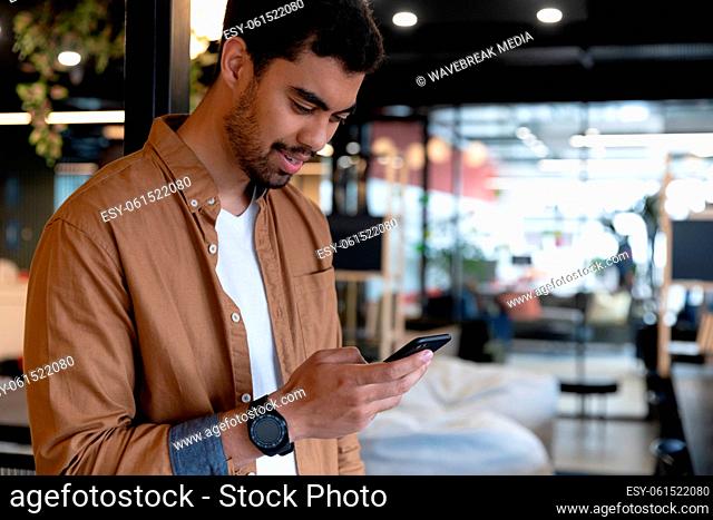 Smiling mixed race businessman texting on smartphone in creative office