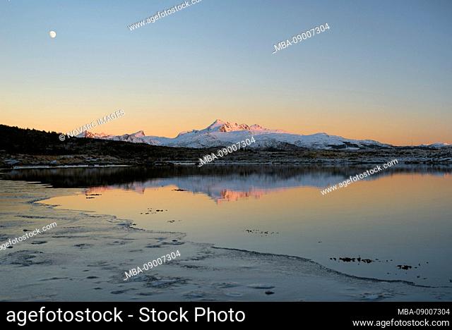 Mountains in the last evening light are reflected in a lake while the moon is in the sky, Lofoten, Nordland, Norway