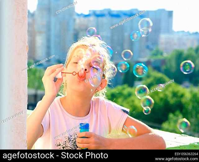 Girl blows a lot of soap bubbles from the balcony of the house