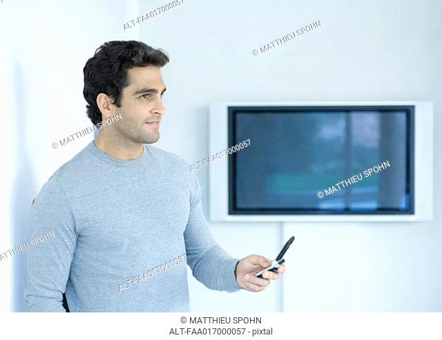 Man holding out cell phone, looking away, widescreen TV in background