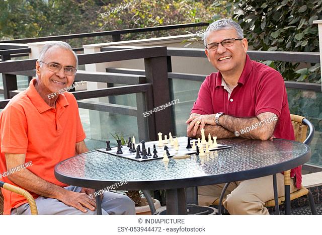 Portrait of senior men smiling while sitting around table with chess board