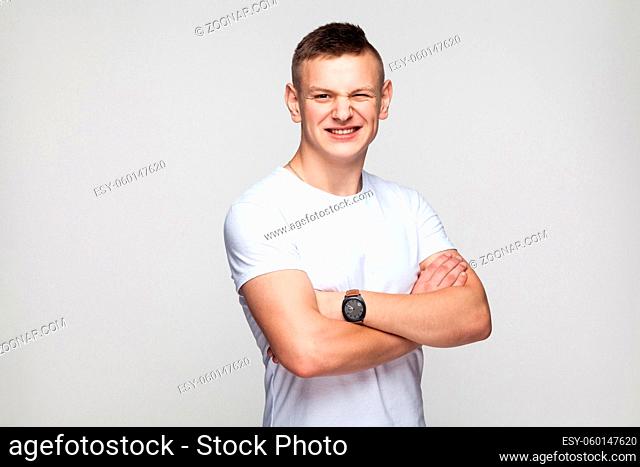 Boy crossed hands toothy smile and wink at camera. Studio shot