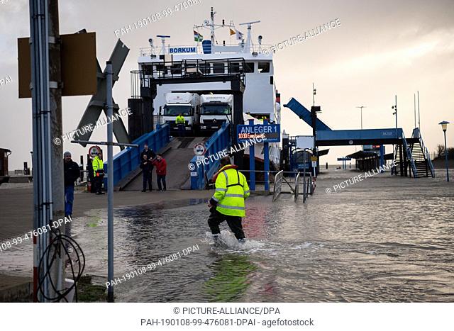 08 January 2019, Lower Saxony, Borkum: During a storm, a worker walks along the flooded area of the ferry port on the North Sea island of Borkum