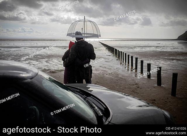 Couple under umbrella on wet stormy winter beach
