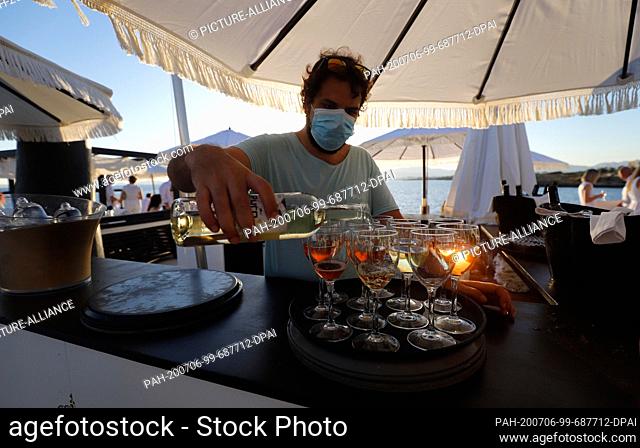 23 June 2020, Spain, Palma: A waiter with a face mask serves wine in glasses at the Bar Purobeach in Cala Estancia on the beach Playa de Palma