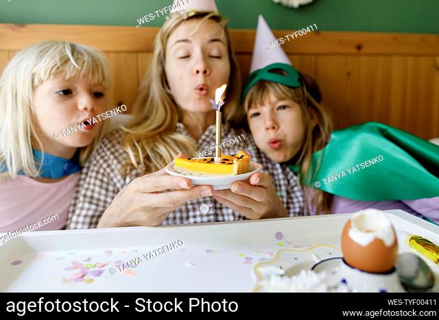 Daughters and mother blowing candles in bedroom