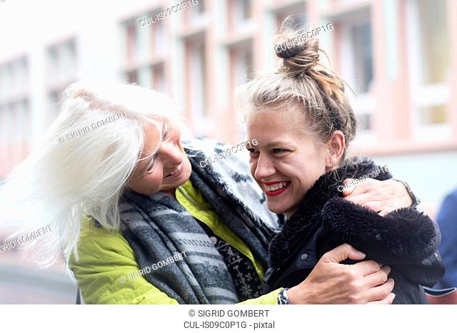 Mature woman and daughter hugging on city street