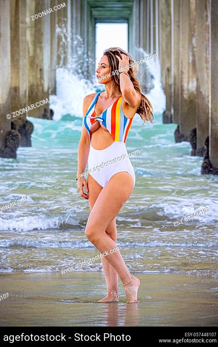 A beautiful brunette bikini model poses under the pier