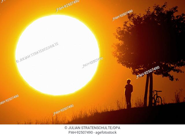 dpatop - A man standing on a hill under a tree is silhouetted against the evening sun in Hanover, Germany, 17 July 2017. Photo: Julian Stratenschulte/dpa |...