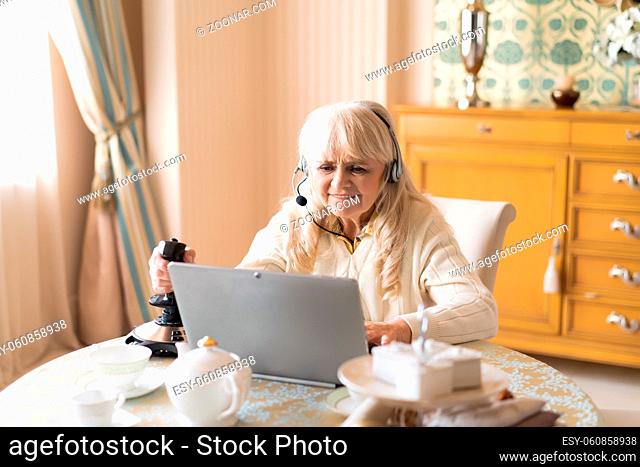 Senior Woman Bites Her Lip While Playing Video Games On Retro Joystick On Her Computer. Playing Video Games Concept