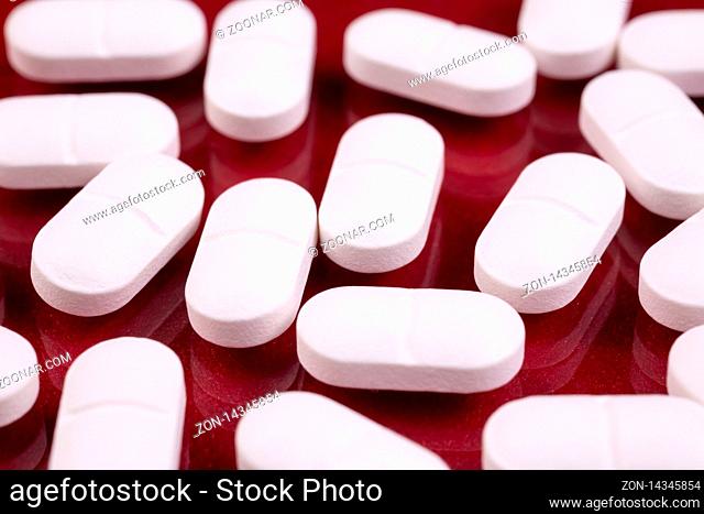 White pills isolated on a red reflective background. Global pharmaceutical industry for billions dollars per year. Pharmaceutical drugs for use as medications