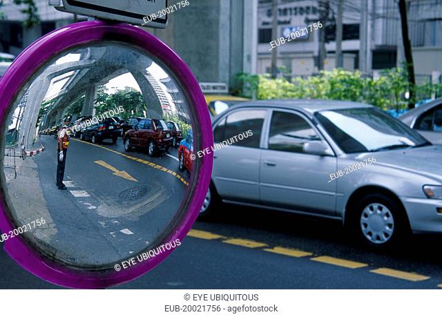Road side mirror reflecting traffic policeman with passing traffic