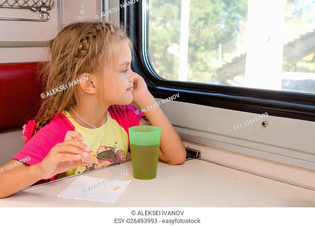 Six-year girl sitting on the train at the table on outboard second-class carriage and enthusiastically looking out the window