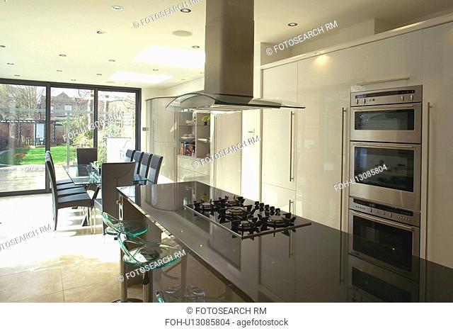 Extractor above hob set into island unit with granite worktop in modern white openplan kitchen and dining room