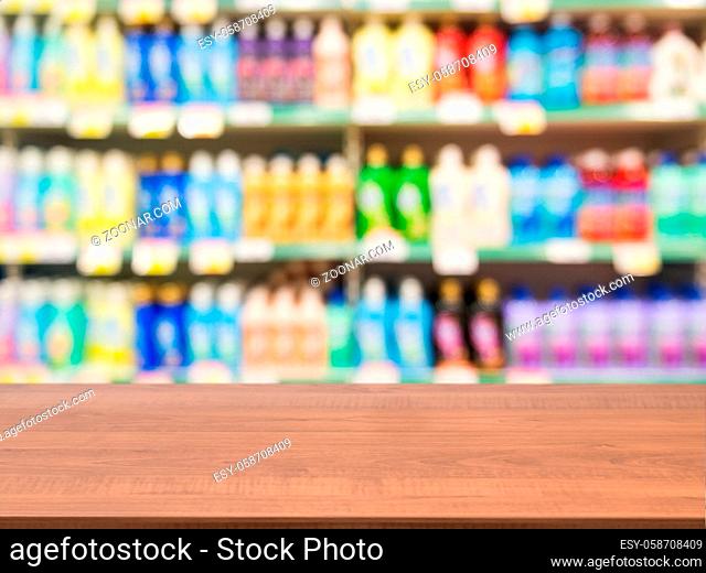 Wooden board empty table in front of blurred background. Perspective dark wood over blur colorful supermarket products on shelves