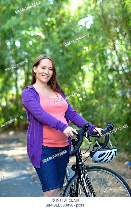 Pregnant Caucasian woman standing with bicycle