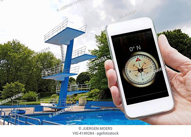 05.06.2013 , Germany , Gladbeck , empty public swimming pool with pool tower, hand holds compass, pointing north ( photomontage )