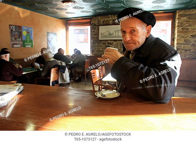 Elderly man takes a coffee in a bar while friends play cards in backgroudn. A Fonsagrada (Lugo)