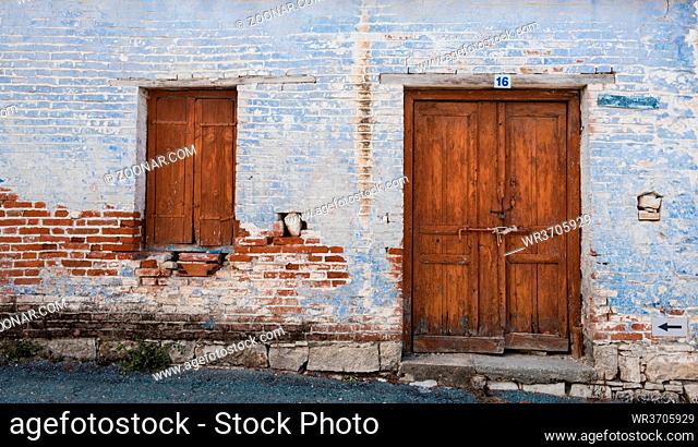 Exterior of an old village house with blue stoned wall and closed vitnage door and window