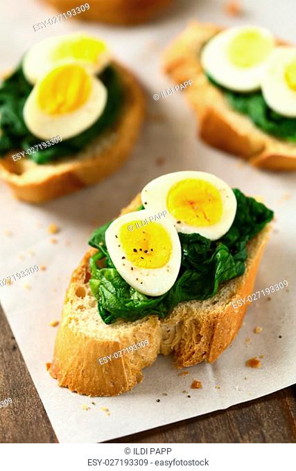 Crostini roasted bread slices with cooked spinach leaves and hard boiled quail eggs seasoned with black pepper, photographed with natural light (Selective Focus