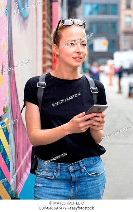 Closeup of female hipster with smart phone. Woman using smart phone app guite on city break weekend trip to East Village, New York city, USA