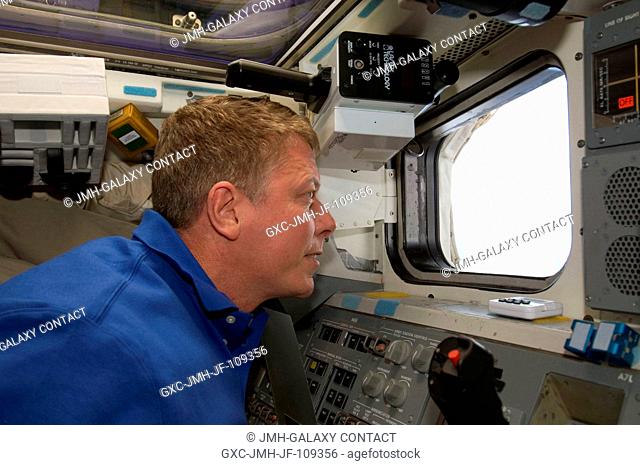 Astronaut Mike Fossum, STS-124 mission specialist, looks through a window on the aft flight deck of Space Shuttle Discovery while docked with the International...